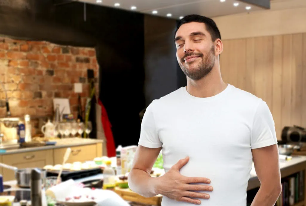 happy full man touching tummy over kitchen